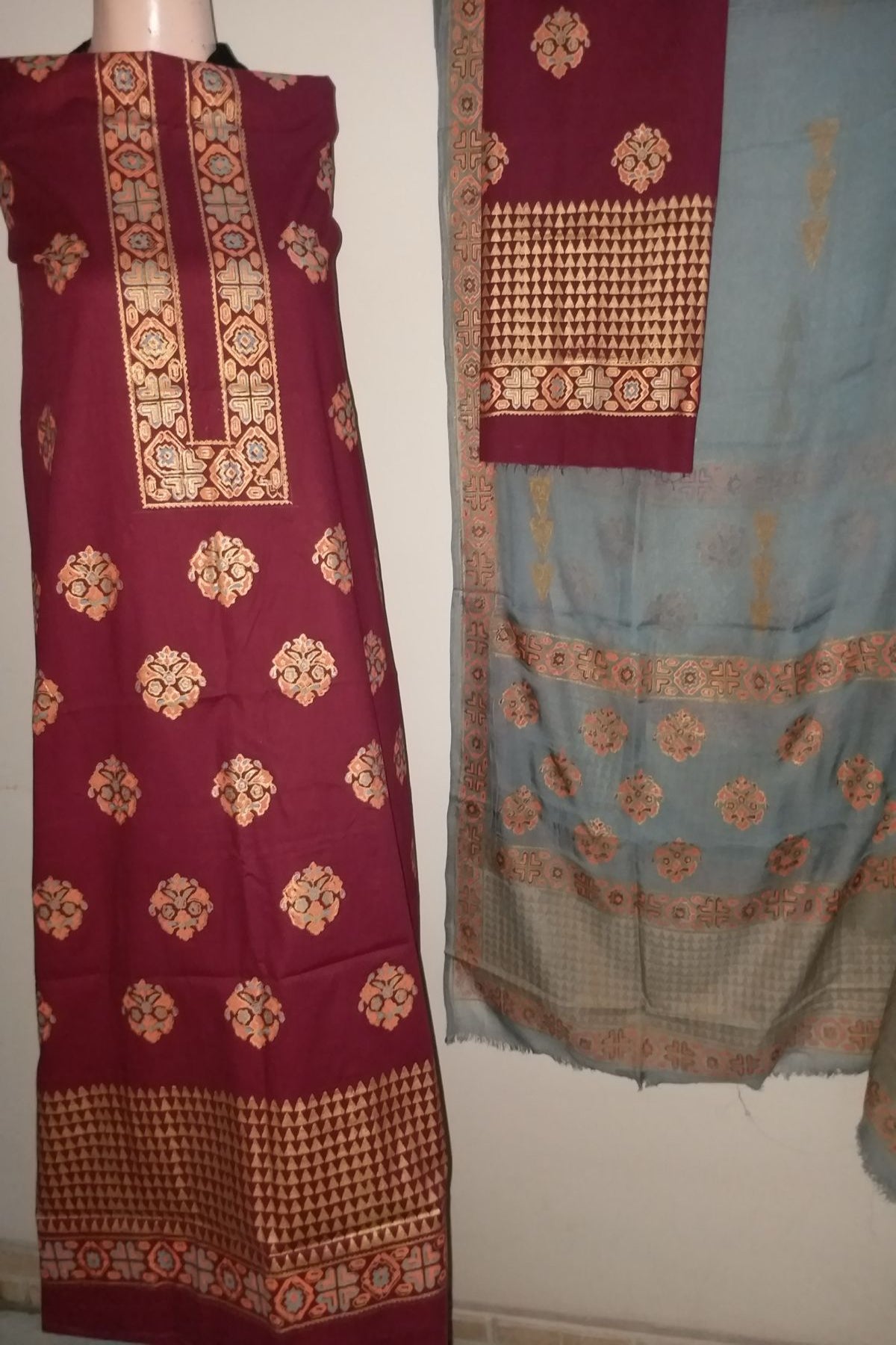 A 3-piece unstitched hand block print suit featuring a deep maroon fine lawn shirt with gold and peach geometric neck and daman borders, paired with a contrasting slate grey chiffon dupatta."
