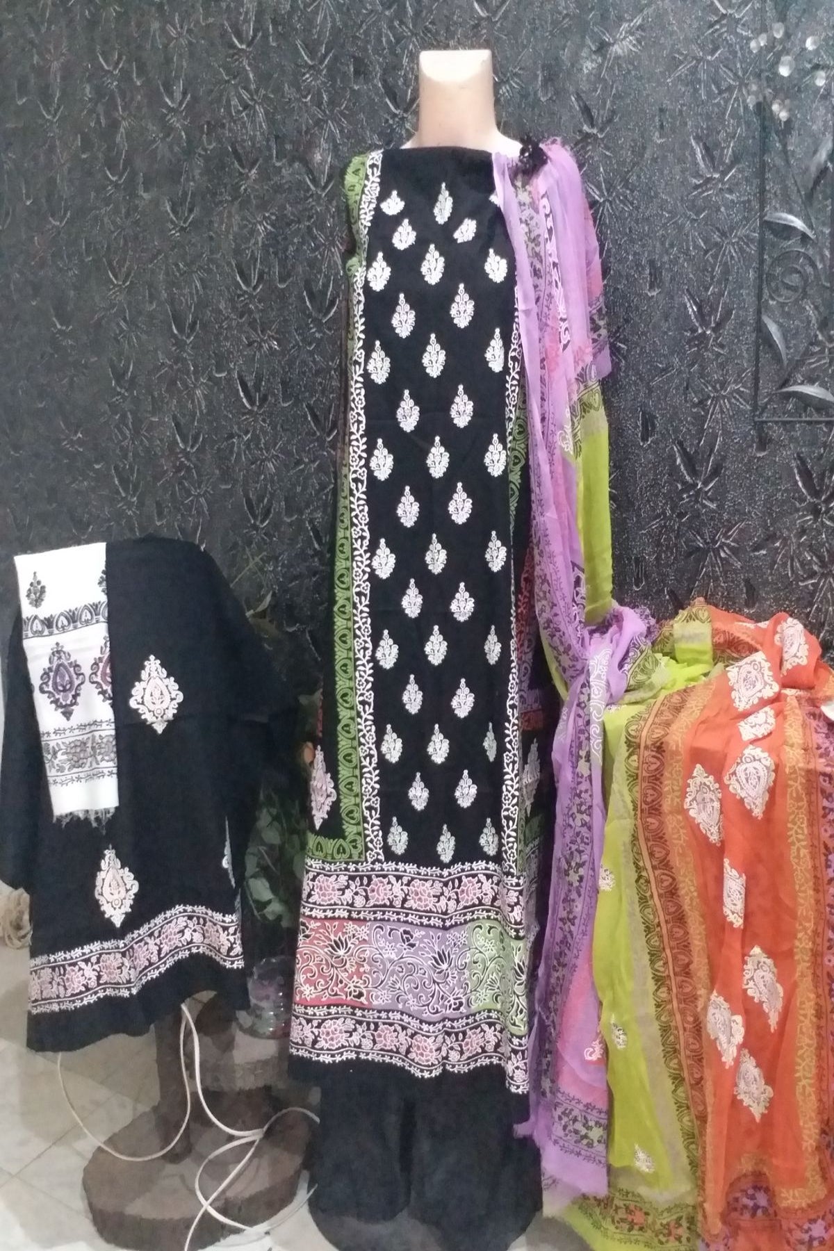 Three-piece unstitched fine lawn suit with a black base and white block prints, decorated with pink and green borders, alongside a colorful chiffon dupatta.