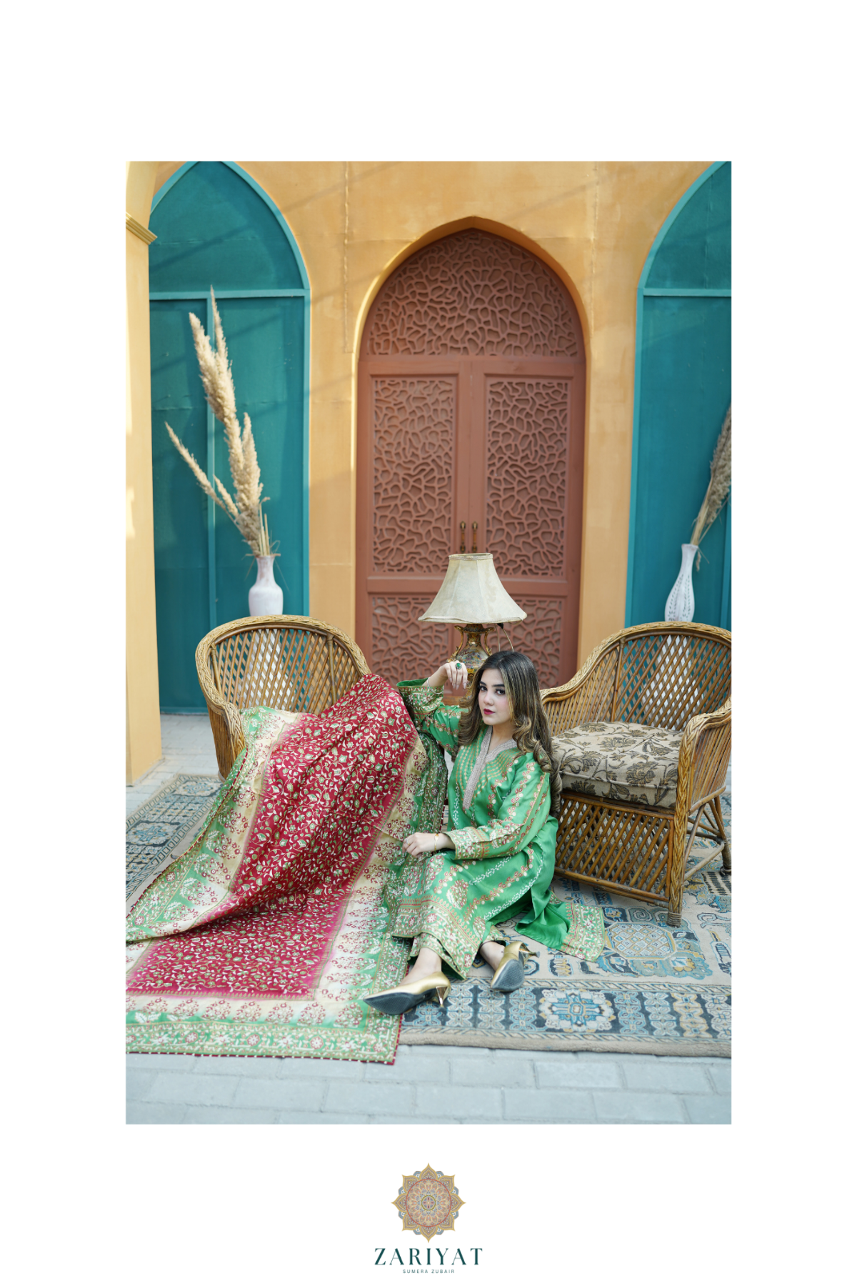 A woman models a green traditional outfit with a red patterned dupatta in an outdoor patio setting with wicker chairs, a carved wooden door, and teal arches. The brand name 'Zariyat' is visible at the bottom of the image.
