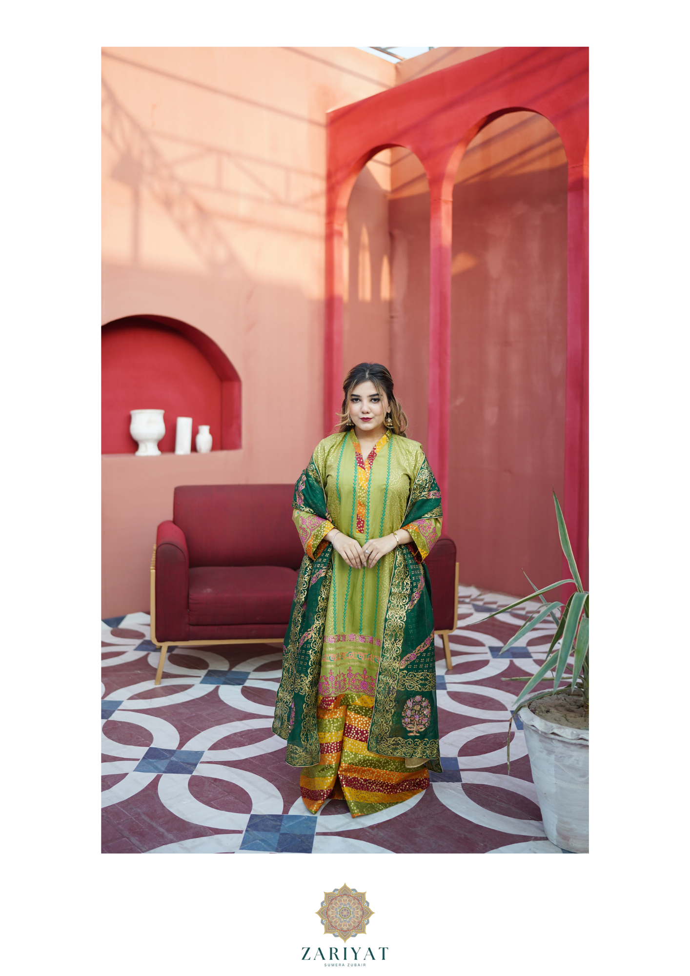 Pakistani lime-green festive suit by Zariyat. Features a printed long kurti, a multi-colored chunri flared lehenga skirt, and a deep green printed dupatta modeled outdoors against a terracotta arched wall.