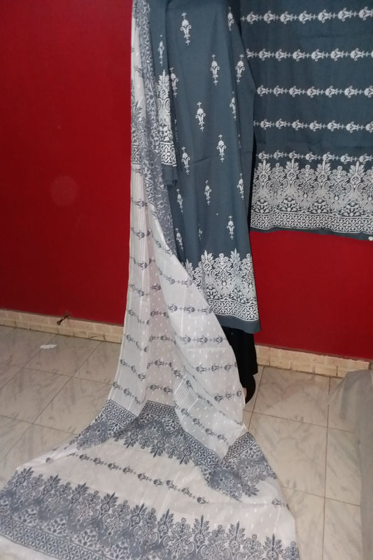 A 3-piece unstitched hand block print suit featuring a dark charcoal grey fine lawn shirt with delicate white floral motifs and an intricate white daman border, paired with a flowing white and grey chiffon dupatta