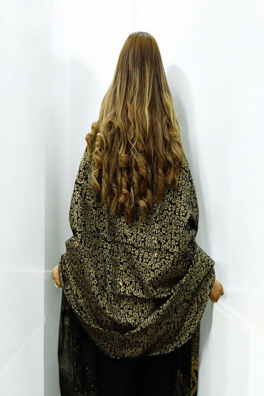 Back view of a woman showcasing a premium black luxury shawl with dense gold zari embroidery and intricate floral jacquard patterns.