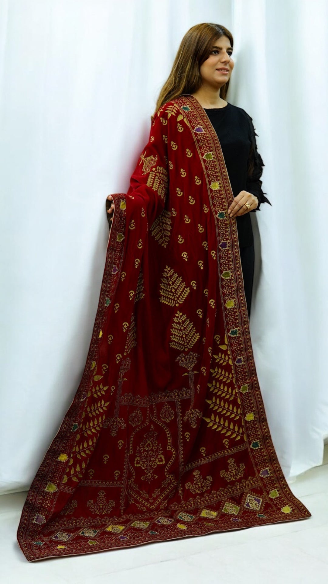 Close-up of a model draping a luxurious Zariyat red velvet shawl featuring intricate gold screen-printed motifs and a fringed gold border.