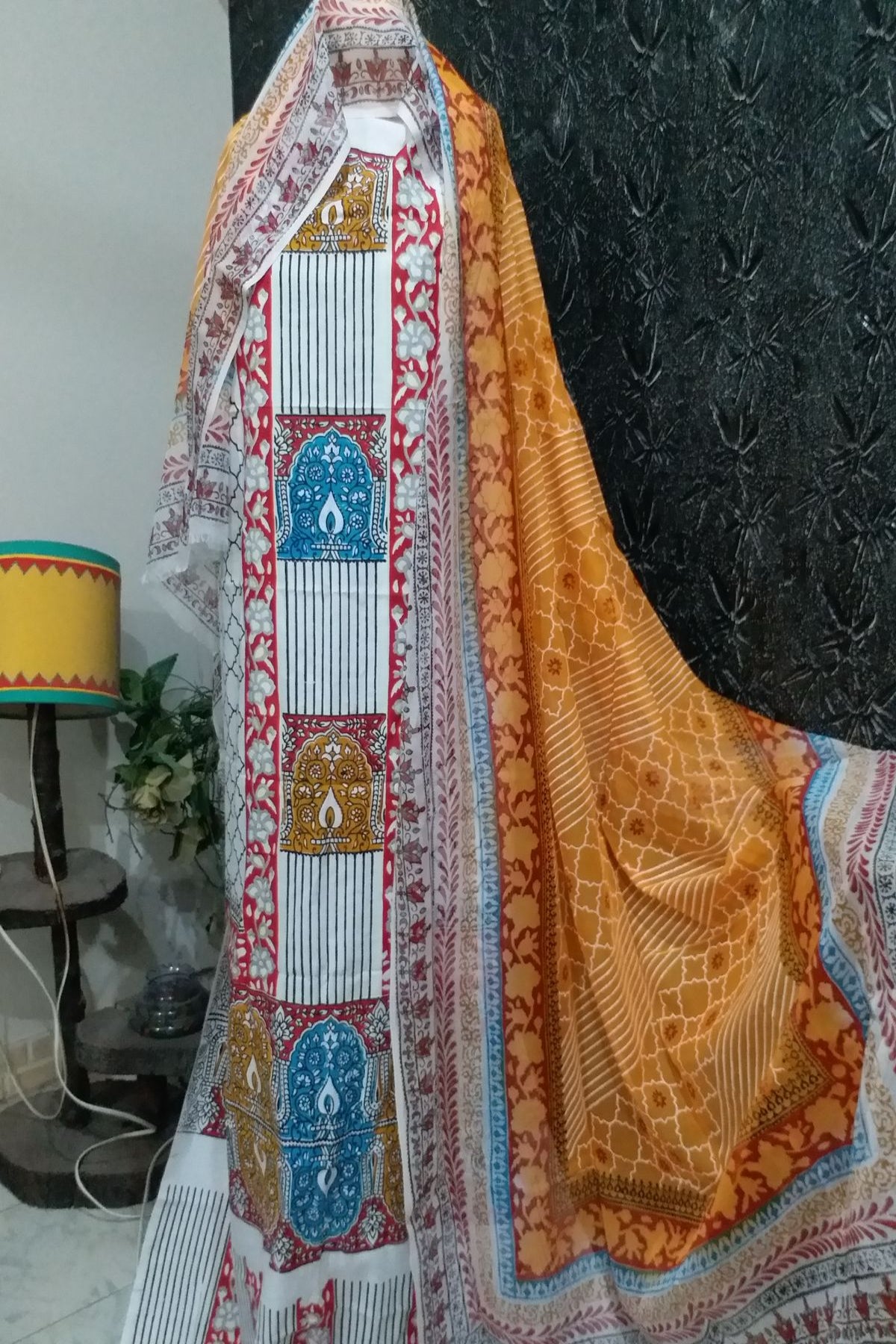 Close-up of a 3-piece unstitched traditional block print suit in white, mustard yellow, and blue patterns on fine lawn fabric with a matching dupatta displayed on a mannequin."