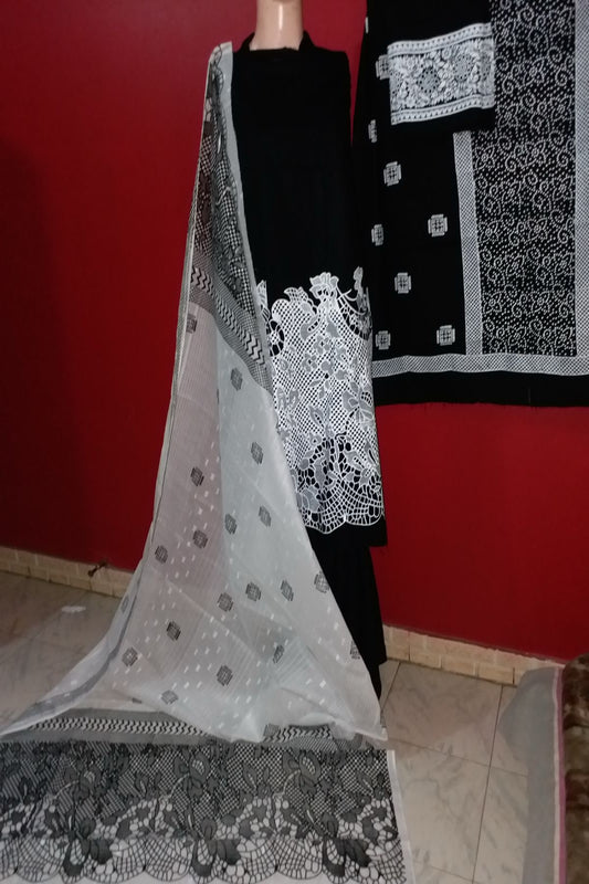 A luxury 3-piece unstitched hand block print suit featuring a jet black fine lawn shirt with bold white lace-like floral daman borders, paired with a sheer white and black chiffon dupatta