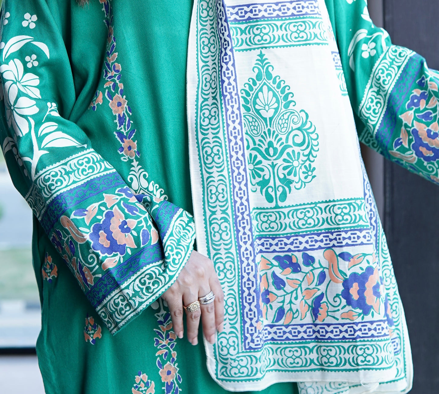 Close up of sleeve design featuring multi color blue and purple floral block print border on a green lawn shirt.