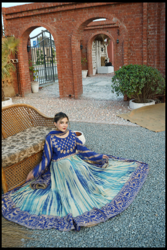 Person wearing a blue and green traditional outfit standing in front of a brick building.