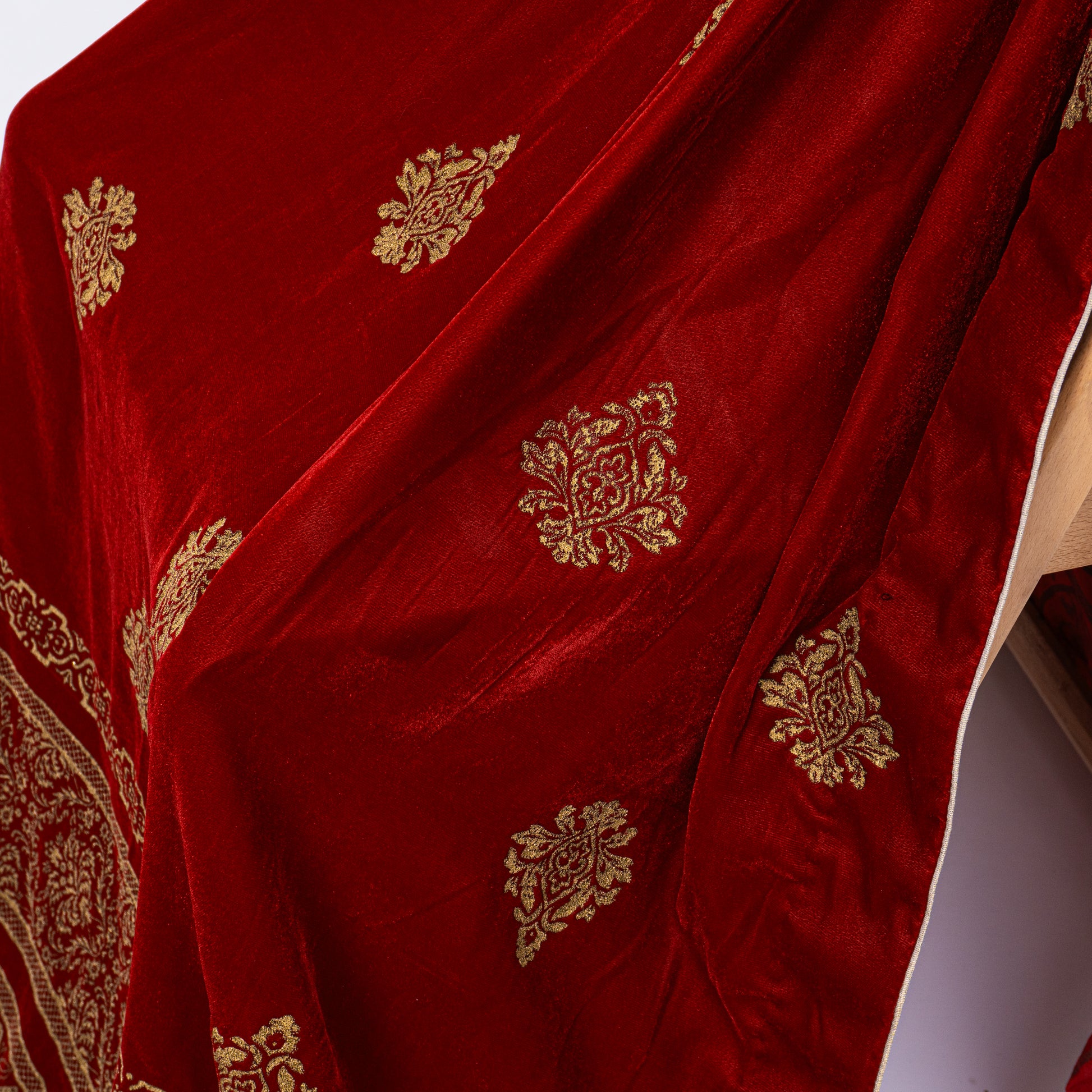 Close-up of golden screen printed traditional motifs scattered across rich maroon velvet fabric