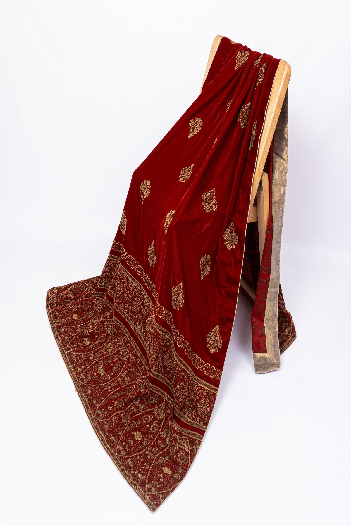Premium maroon velvet shawl with heavy golden screen print border draped on a chair, showcasing luxury winter festive wear
