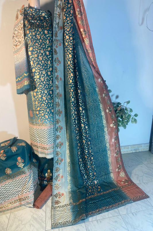 Three-piece unstitched teal and peach fine raw silk suit featuring intricate gold block printing and geometric patterns alongside a matching fine medium silk dupatta.