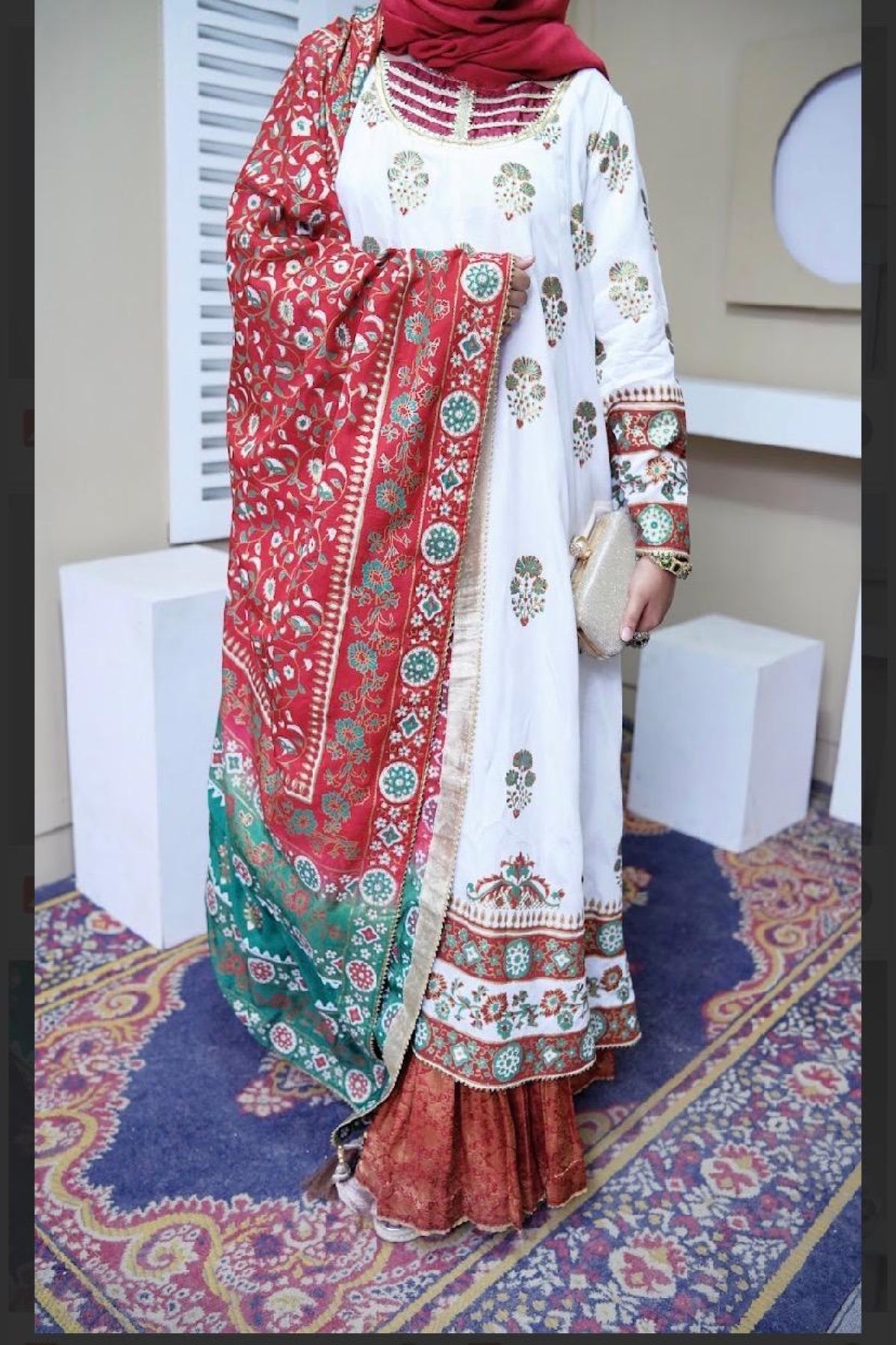 Flat lay of a white and maroon raw silk stitched 2-piece block print kalidar frock paired with a red and green shaded dupatta and golden zari details.