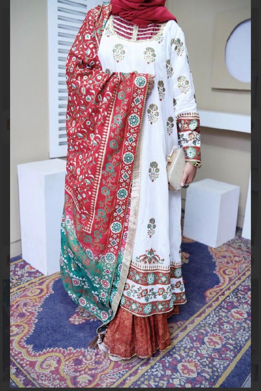 Flat lay of a white and maroon raw silk stitched 2-piece block print kalidar frock paired with a red and green shaded dupatta and golden zari details.